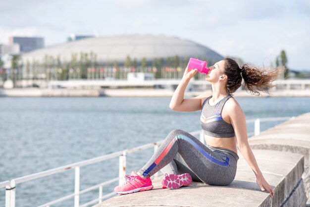 Mujer bastante deportiva bebiendo por el río de la ciudad