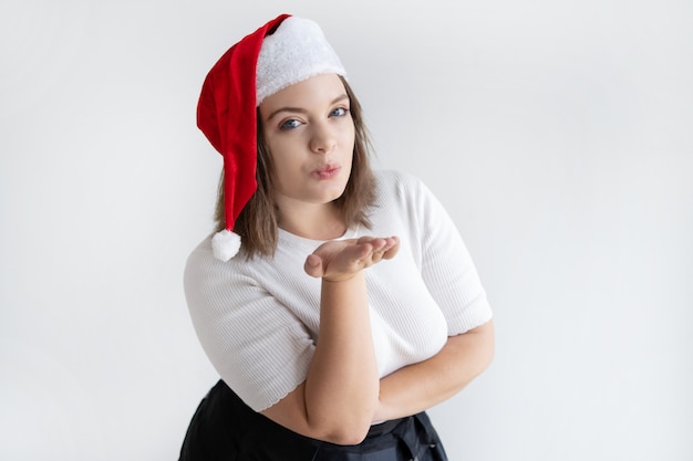 Mujer bastante joven en el beso que sopla del sombrero de Papá Noel