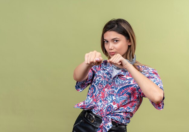 Una mujer bastante joven confiada en camisa estampada de paisley usando audífonos mostrando movimientos de boxeo