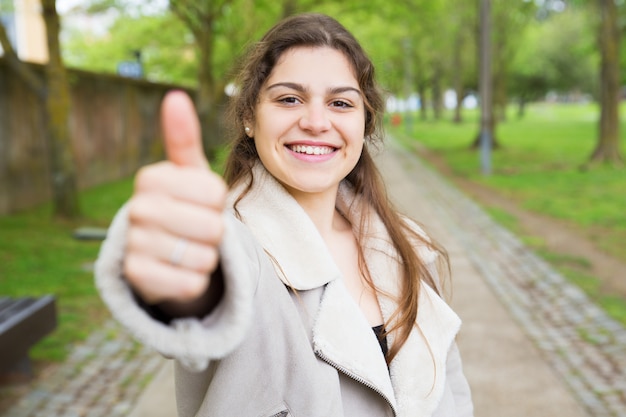 Mujer bastante joven feliz que muestra el pulgar para arriba en parque