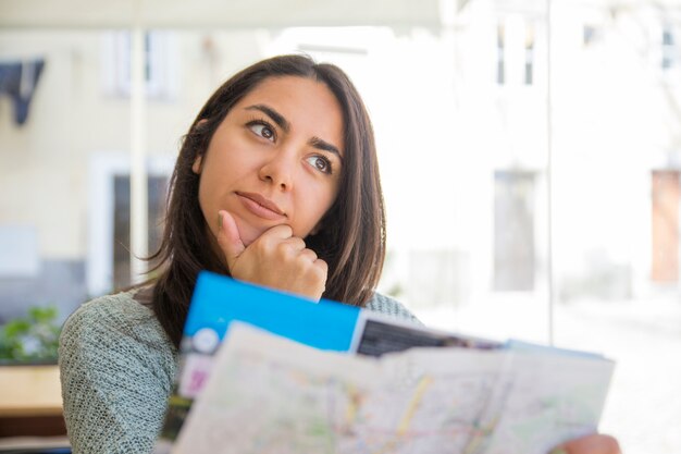 Mujer bastante joven soñadora que usa el mapa de papel en café