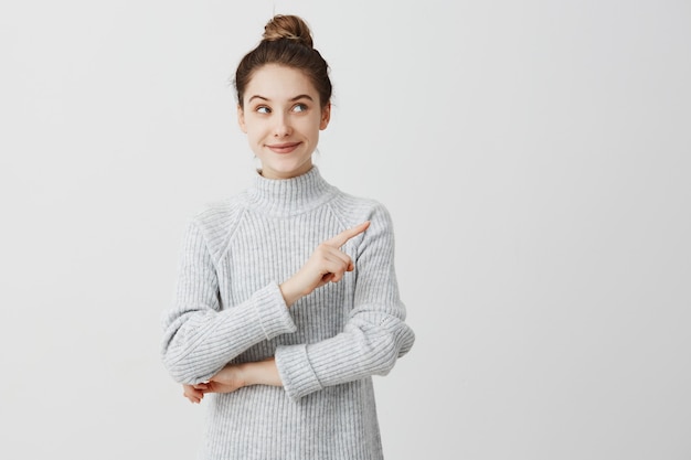 Mujer bastante morena que presenta con mirada difícil y que gesticula al lado. Diseñador femenino que presenta un producto encantador con el dedo índice. Concepto de gesto