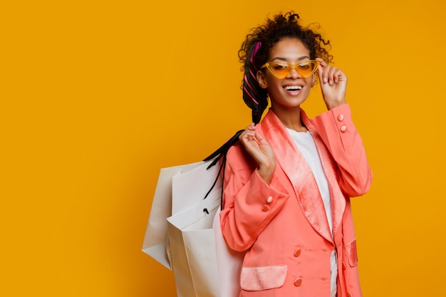 Mujer bastante negra con el bolso de compras blanco que se coloca sobre fondo amarillo. Primavera de moda look de moda.