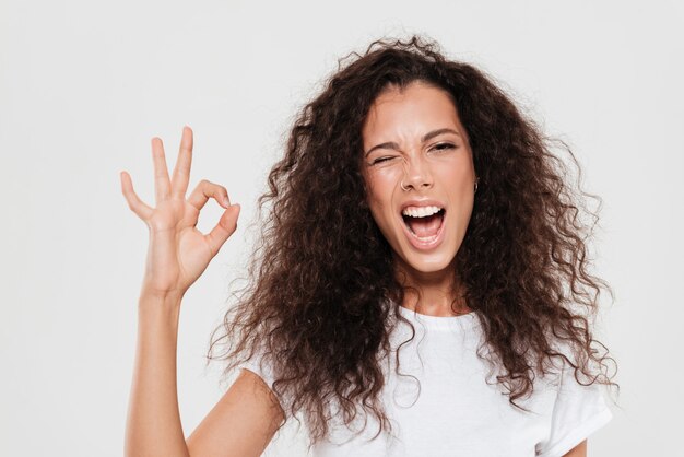 Mujer bastante rizada mostrando signo bien con la boca abierta