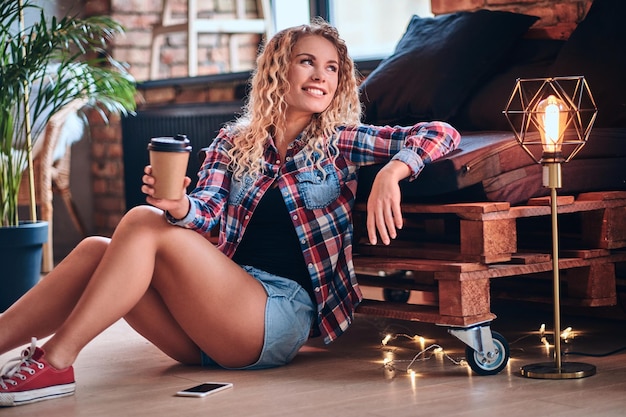 Mujer bastante rubia hipster bebe café por la mañana en un baño con interior de loft.