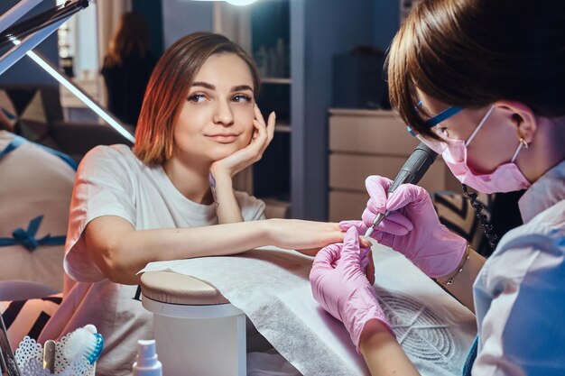 Mujer bastante soñadora con tatuaje recibió cuidado de uñas de un joven manicurista diligente.