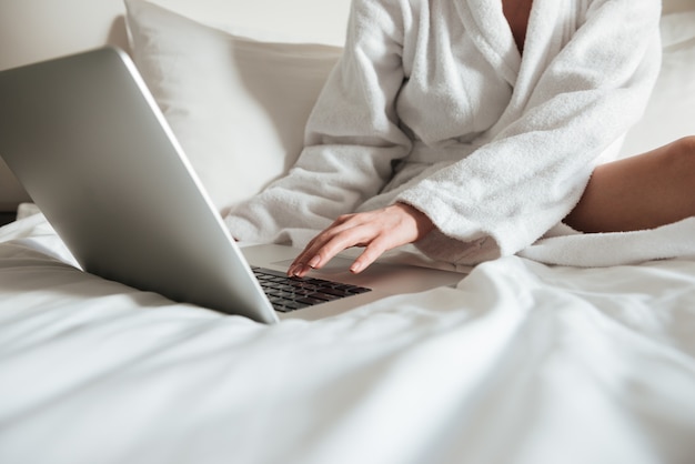 mujer en bata de baño en la cama y usando laptop