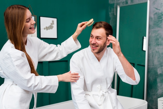 Mujer en bata de baño cepillando el cabello del hombre