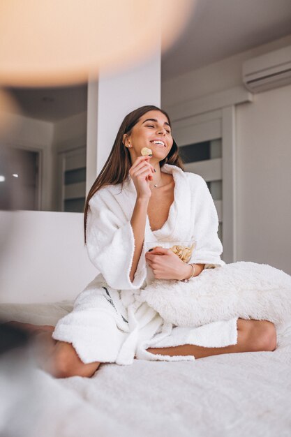 Mujer en bata de baño comiendo cereal en la cama