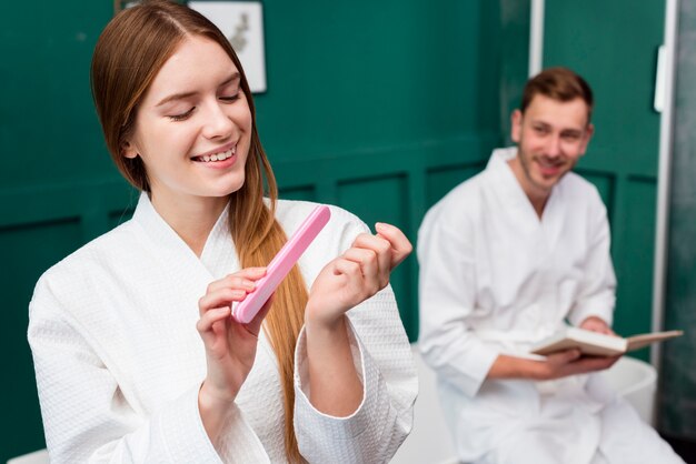 Mujer en bata de baño limándose las uñas