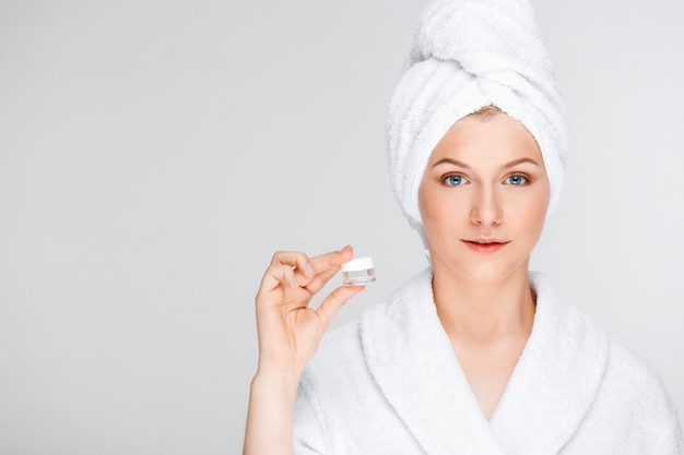 mujer en bata de baño mostrando crema, esencia de elevación de ojos