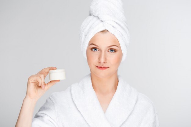 Mujer en bata de baño mostrando crema, producto de cuidado de la piel promo