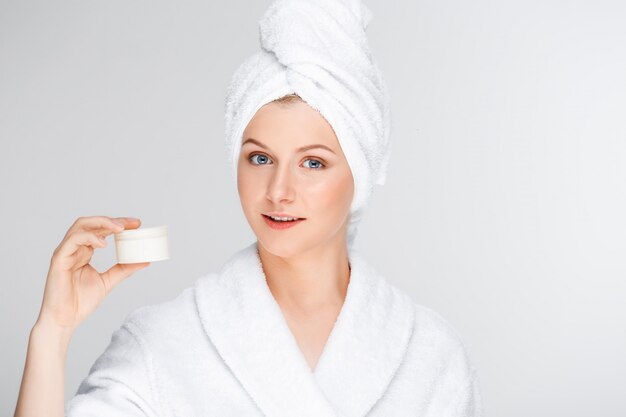 Mujer en bata de baño mostrando crema, producto de cuidado de la piel promo