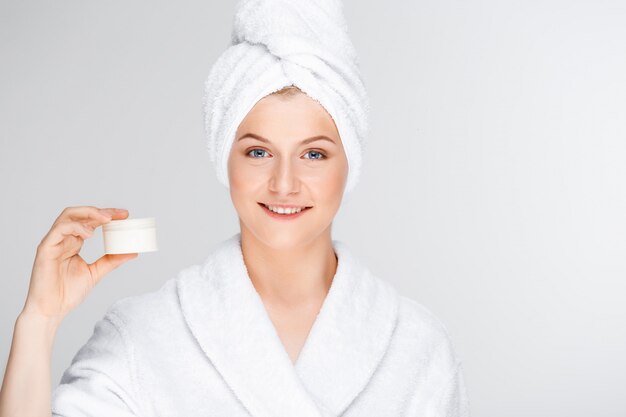 Mujer en bata de baño mostrando crema, producto de cuidado de la piel promo