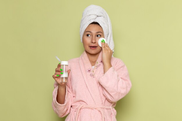 Mujer en bata de baño rosa limpiando todo el maquillaje de su rostro