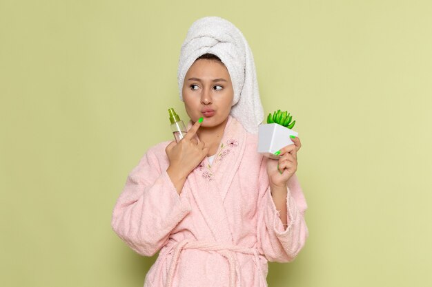 Mujer en bata de baño rosa sosteniendo frasco de spray y planta