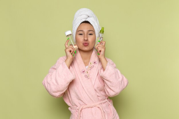 Mujer en bata de baño rosa sosteniendo frascos de spray