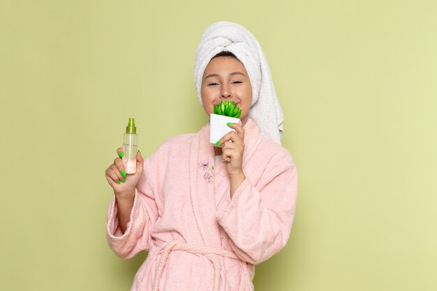 mujer en bata de baño rosa sosteniendo maquillajes spray flas y planta