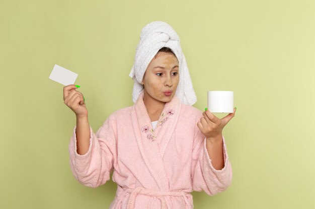 Mujer en bata de baño rosa con tarjeta blanca y crema