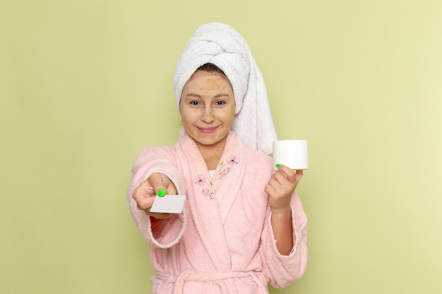 Mujer en bata de baño rosa con tarjeta blanca y crema