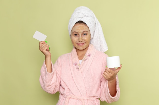 Mujer en bata de baño rosa con tarjeta blanca y crema