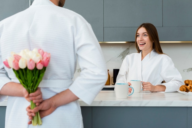 Mujer en bata de baño sorprendida con ramo de tulipanes por hombre