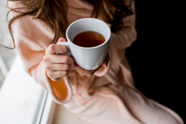 Mujer en bata de baño sosteniendo una taza de té caliente. Estado de ánimo de otoño.