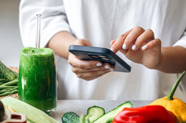 Una mujer con un batido de desintoxicación verde y usando una aplicación de nutrición en su teléfono inteligente