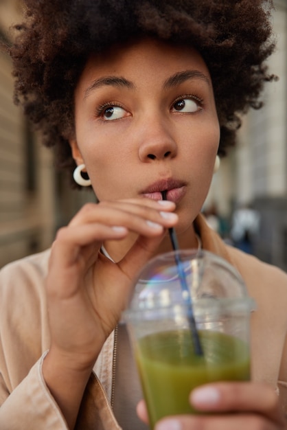 Mujer bebe batido de pepino verde de paja vestidos de chaqueta de moda mira lejos stands