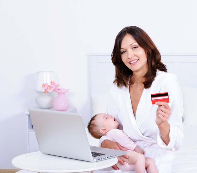 Mujer con bebé, tarjeta de crédito y portátil en casa