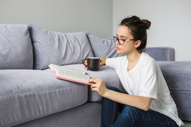 Mujer con bebida leyendo el libro cerca del sofá