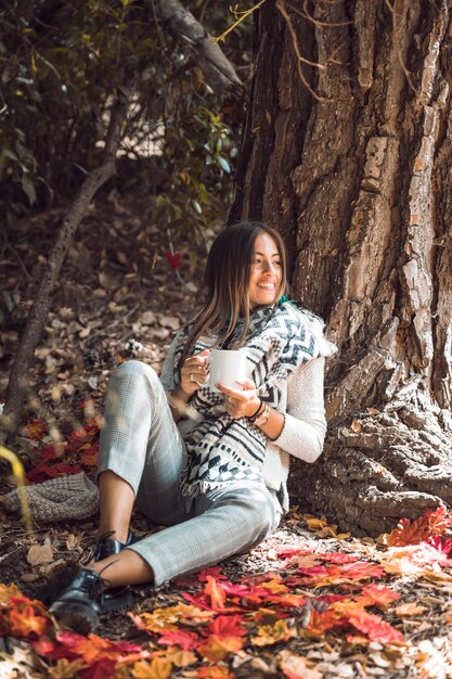 Mujer con bebida mirando a otro lado en el bosque de otoño