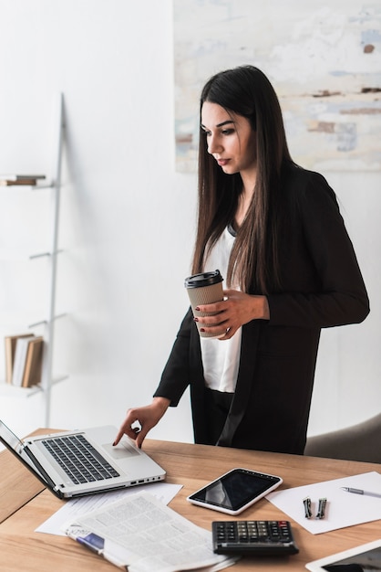 Mujer con bebida usando laptop