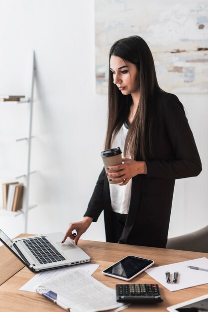 Mujer con bebida usando laptop