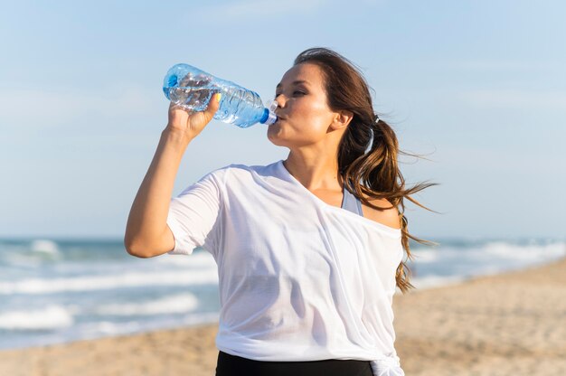 Mujer bebiendo agua en la playa mientras hace ejercicio