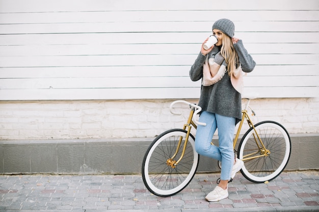 Mujer bebiendo bebida caliente cerca de bicicleta