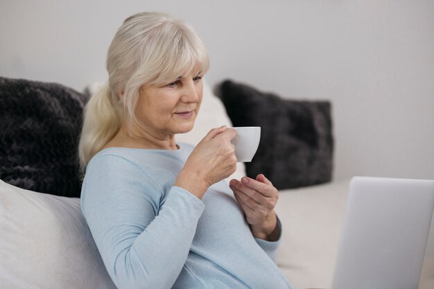 Mujer bebiendo bebida caliente y usando la computadora portátil