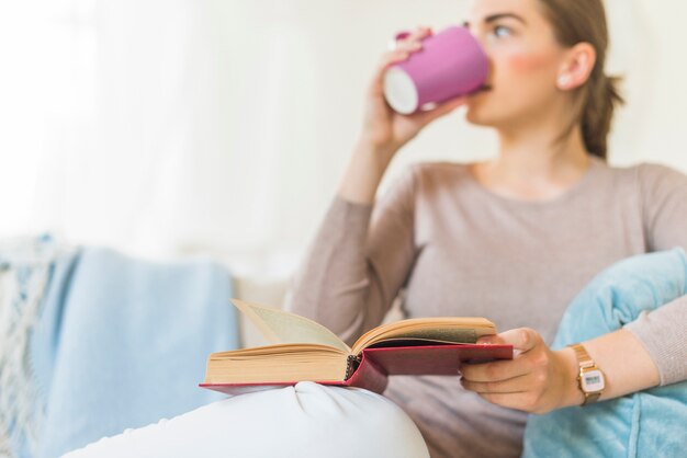 Mujer bebiendo café en casa sosteniendo el libro