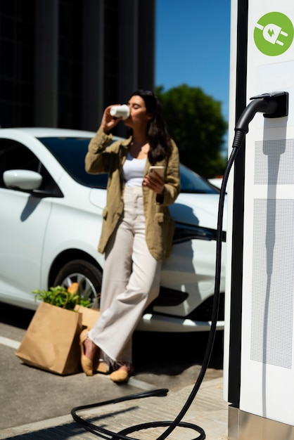 Mujer bebiendo café junto al auto tiro completo