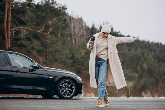 Mujer bebiendo café junto a su coche de pie en la carretera en el bosque