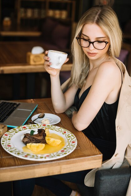 Mujer bebiendo café con postre en la mesa