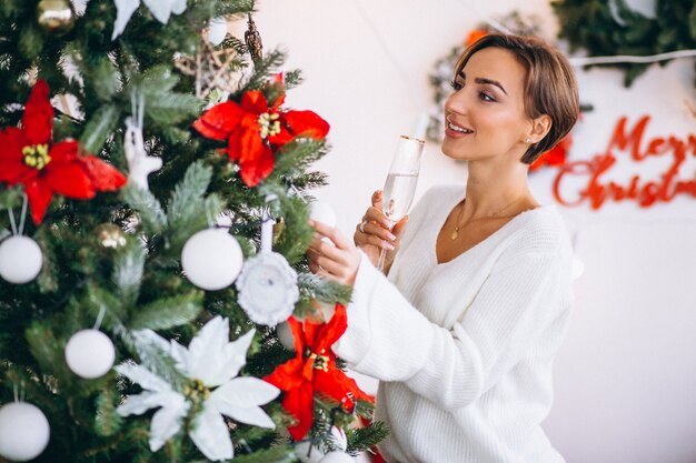 Mujer bebiendo champaigne por arbol de navidad