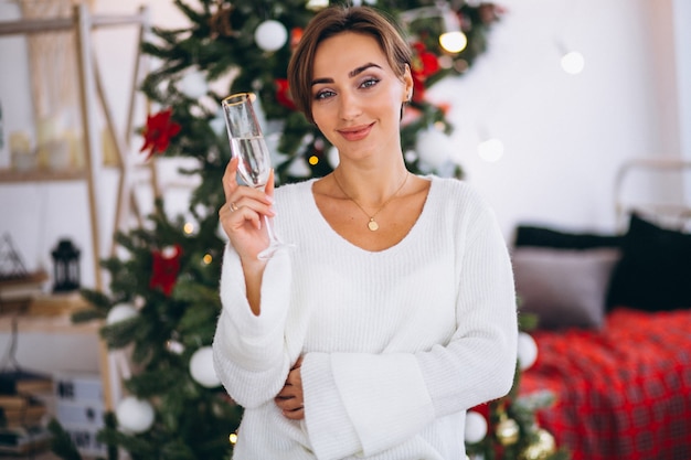 Mujer bebiendo champaigne por arbol de navidad