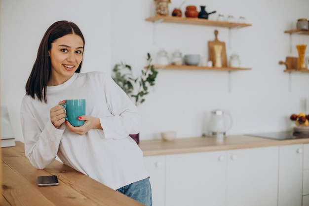 Mujer bebiendo una taza de café en la cocina de casa