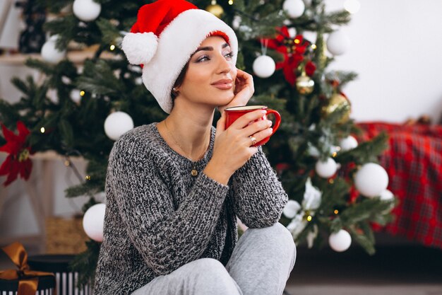 Mujer bebiendo té junto al árbol de navidad