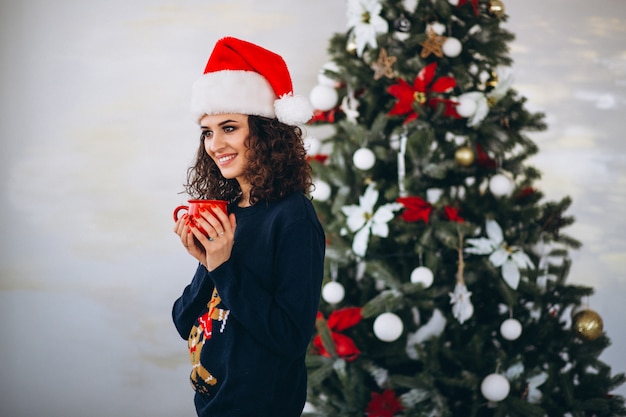 Mujer bebiendo té junto al árbol de navidad