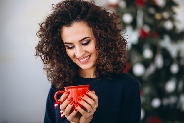 Mujer bebiendo té junto al árbol de navidad