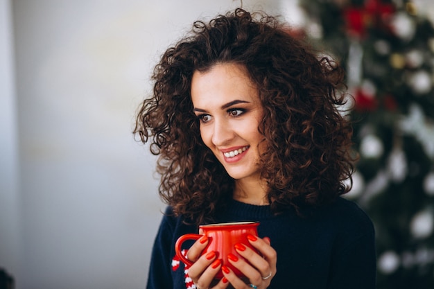 Mujer bebiendo té junto al árbol de navidad