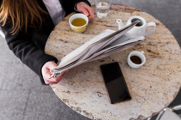 Mujer bebiendo té y leyendo periódico en la mesa