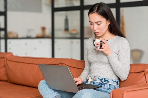 Mujer bebiendo té y usando laptop